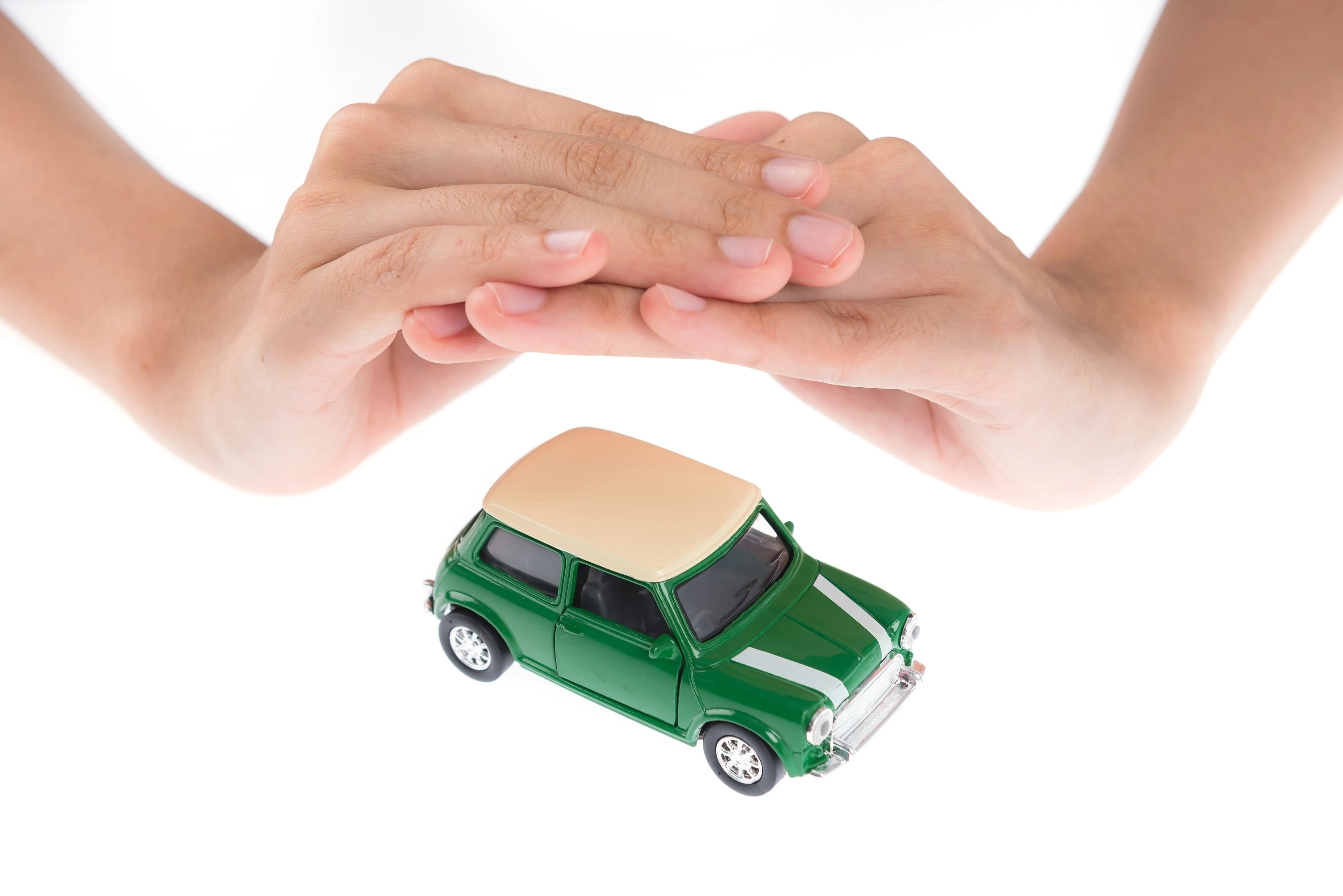 Hände schützen grünes Modellauto, Symbol für Kfz-Versicherung und Sicherheit