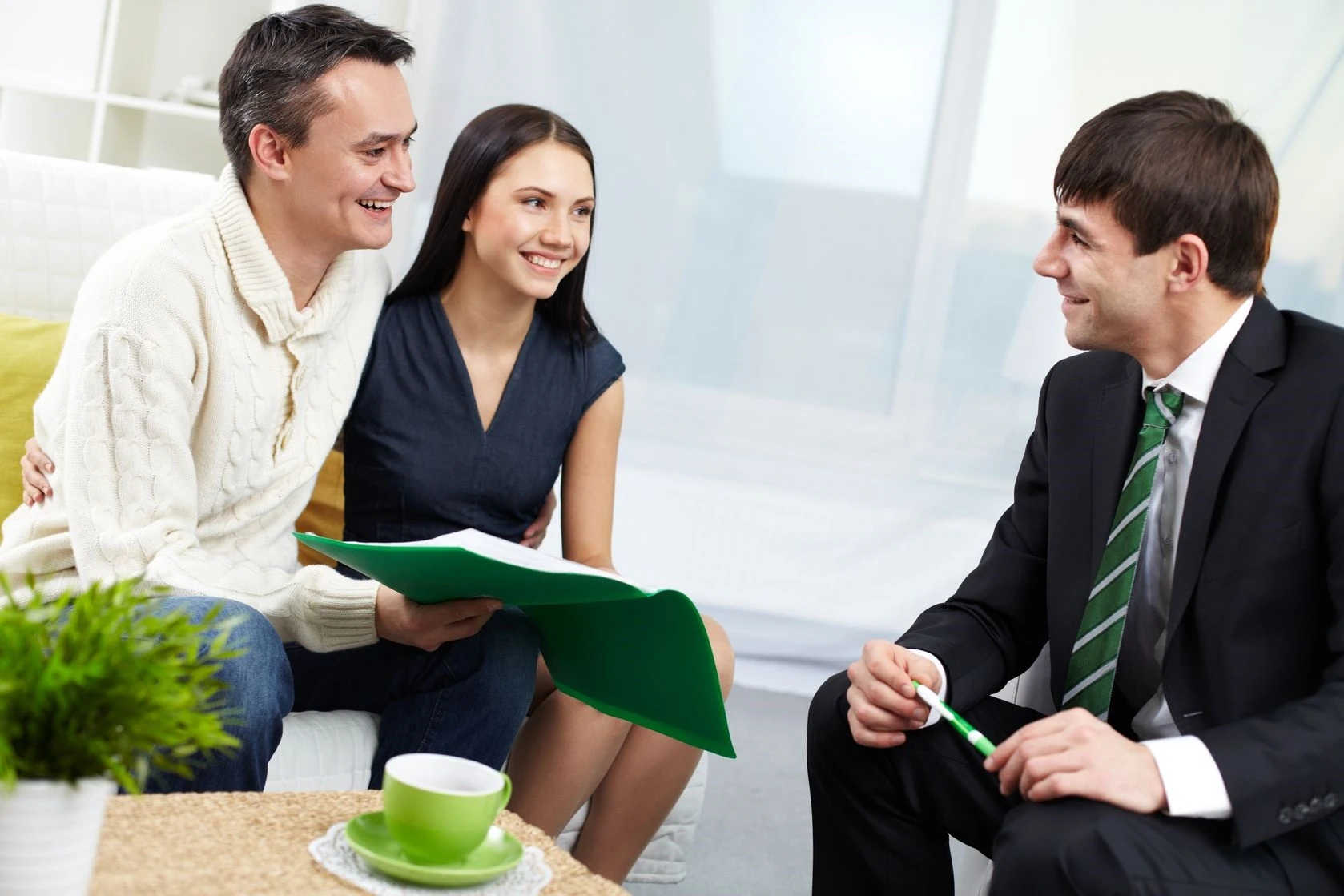 Paar im Beratungsgespräch mit Finanzberater, Unterlagen in grüner Mappe
